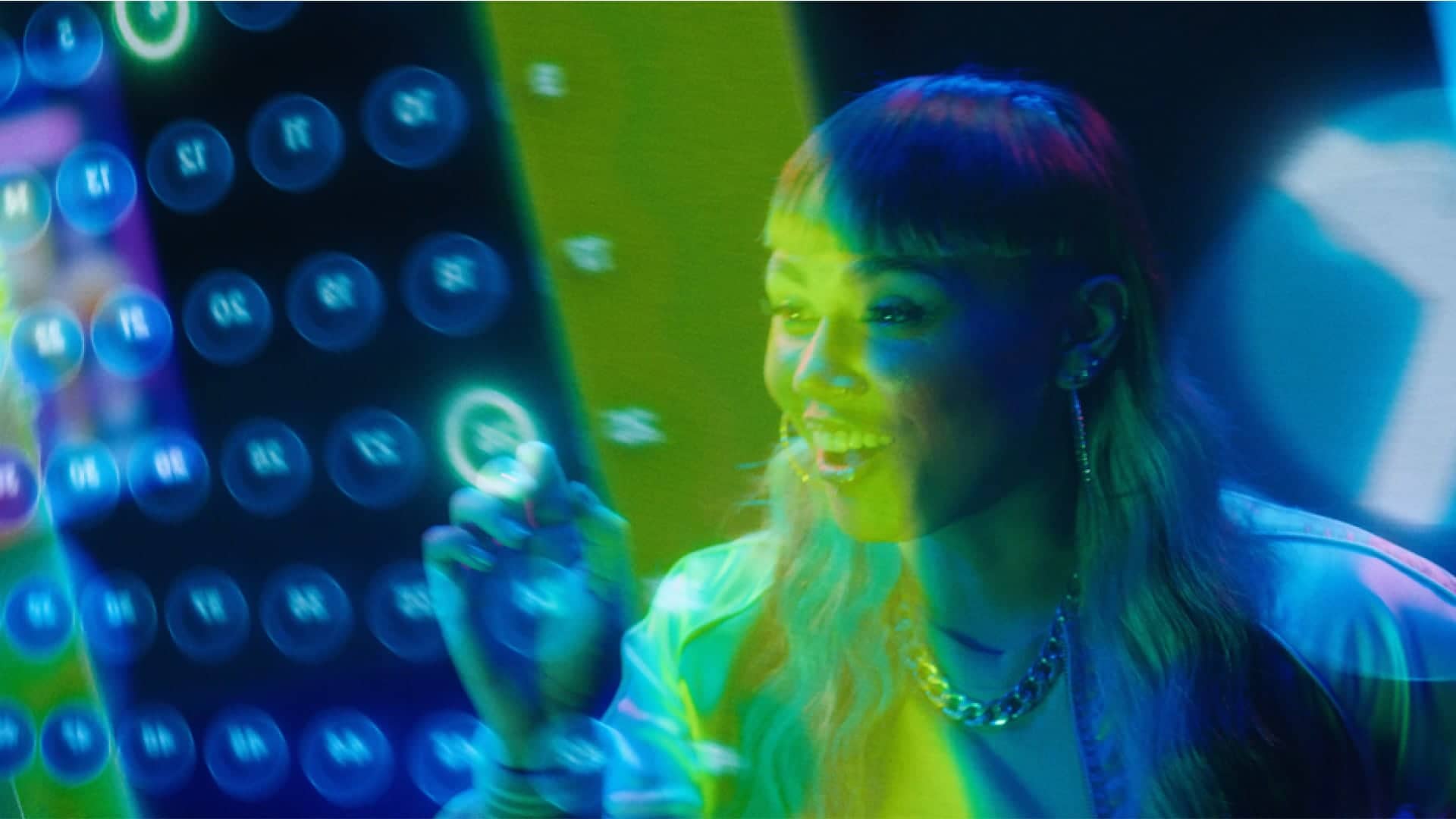 A woman interacts with a futuristic, neon-lit touch screen displaying circular icons and numbers, in a vibrant, tech-themed setting.